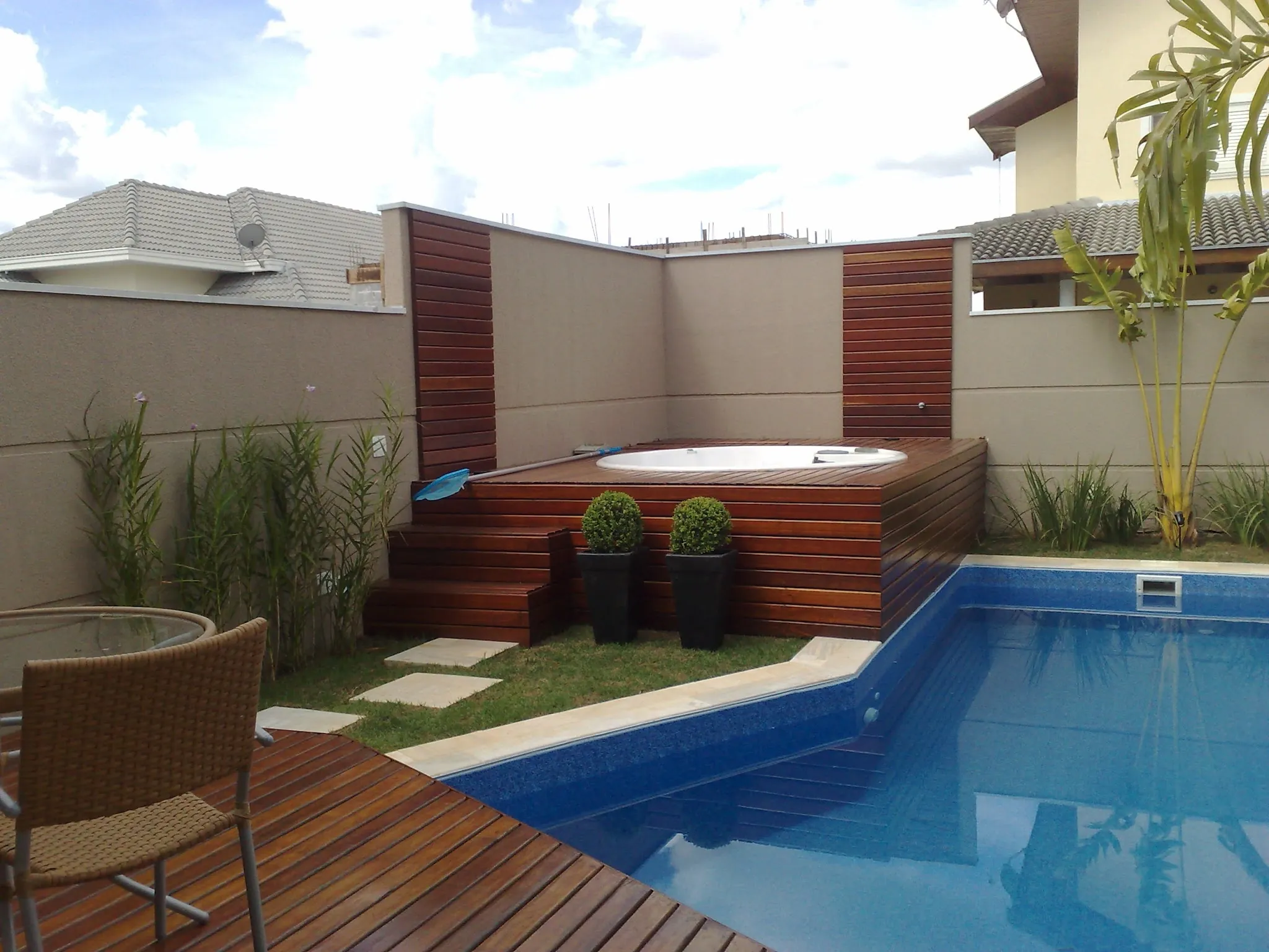 Área de piscina com deck de madeira e canteiros, da Santa Flora Garden